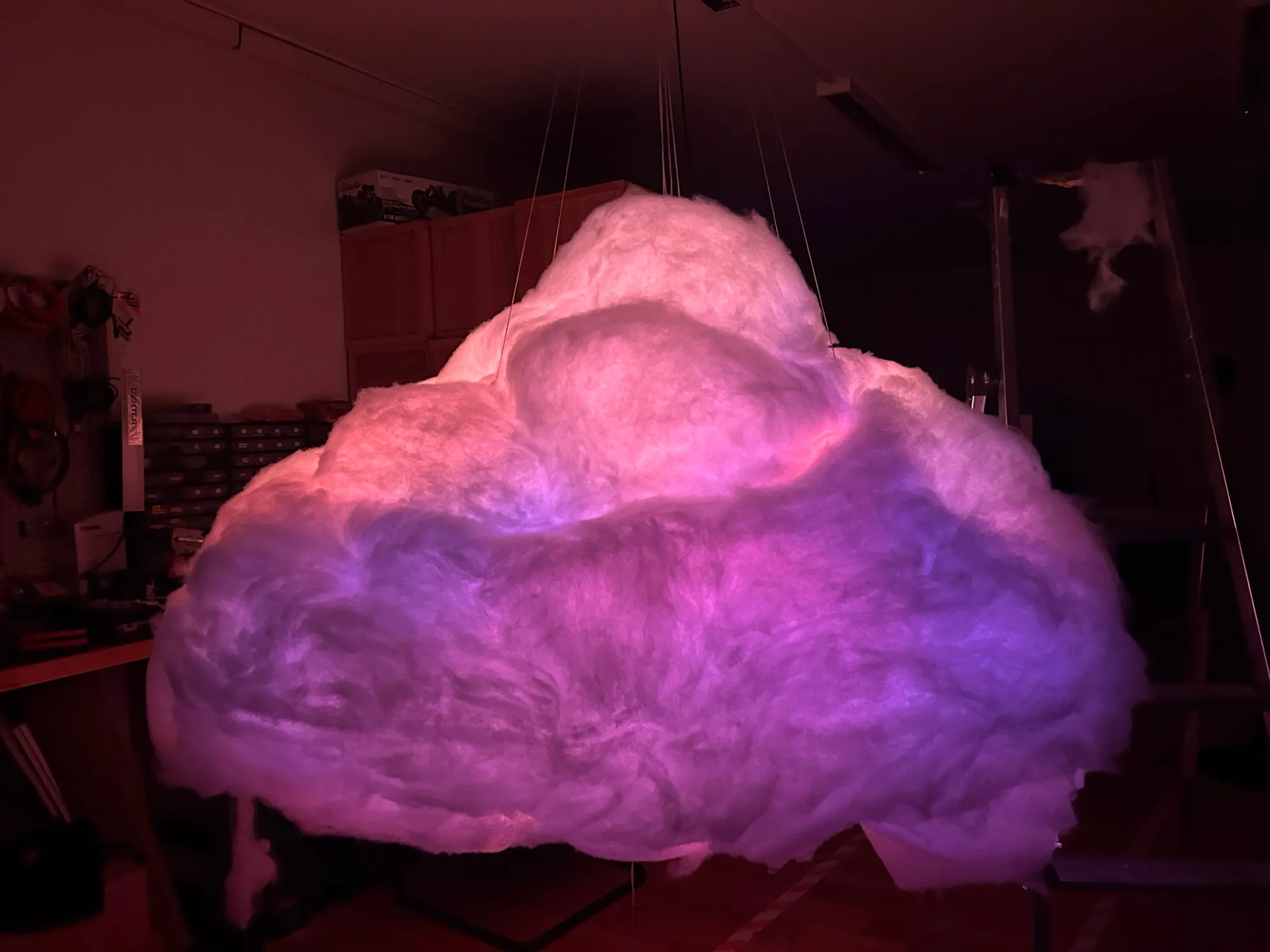 The cloud glowing lilac and pink in the workshop, brightest along its top.